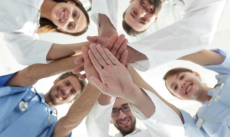 An older couple sits together; the woman uses supplemental oxygen and rests her hand on her chest with her eyes gently closed, conveying calm and strength. Beside her, the man looks at her with a tender expression.