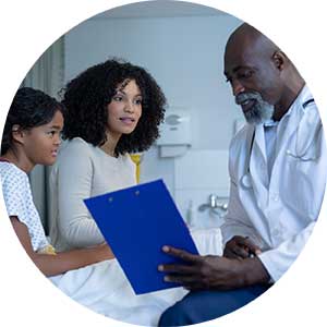 A woman and a young girl talk to a man in a white coat by a hospital bed