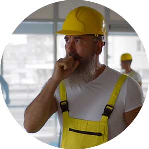 A man in a hard hat in a dusty room coughing