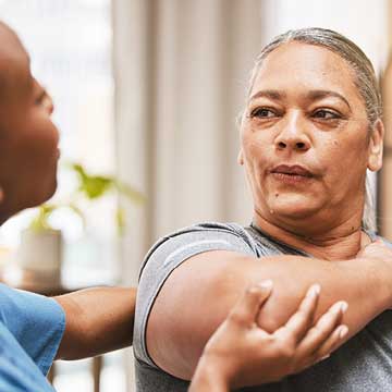 A woman in blue scrubs assists another woman with breath exercises